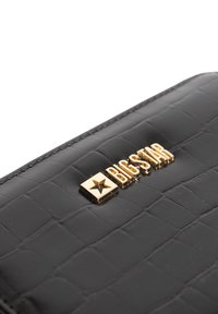 Juodas krokodilo odos tekstūros piniginė su auksinėmis detalėmis, ant lygaus fono iškeltomis raidėmis su "BIG STAR" logotipu ir žvaigždutės akcentu.