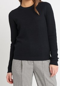 Svart, strukturerad stickad tröja med rund halsringning och långa ärmar, matchad med rutiga, högmidjade byxor.