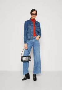 Denim jacket, red turtleneck, wide-leg blue jeans, black heeled boots, and a small black textured handbag. Minimalist design, structured fit.