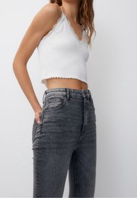 Biały prążkowany krótki top z koronkową lamówką, zestawiony z szarymi dżinsami o wysokim stanze, lekko spranym wyglądzie i bocznymi kieszeniami.