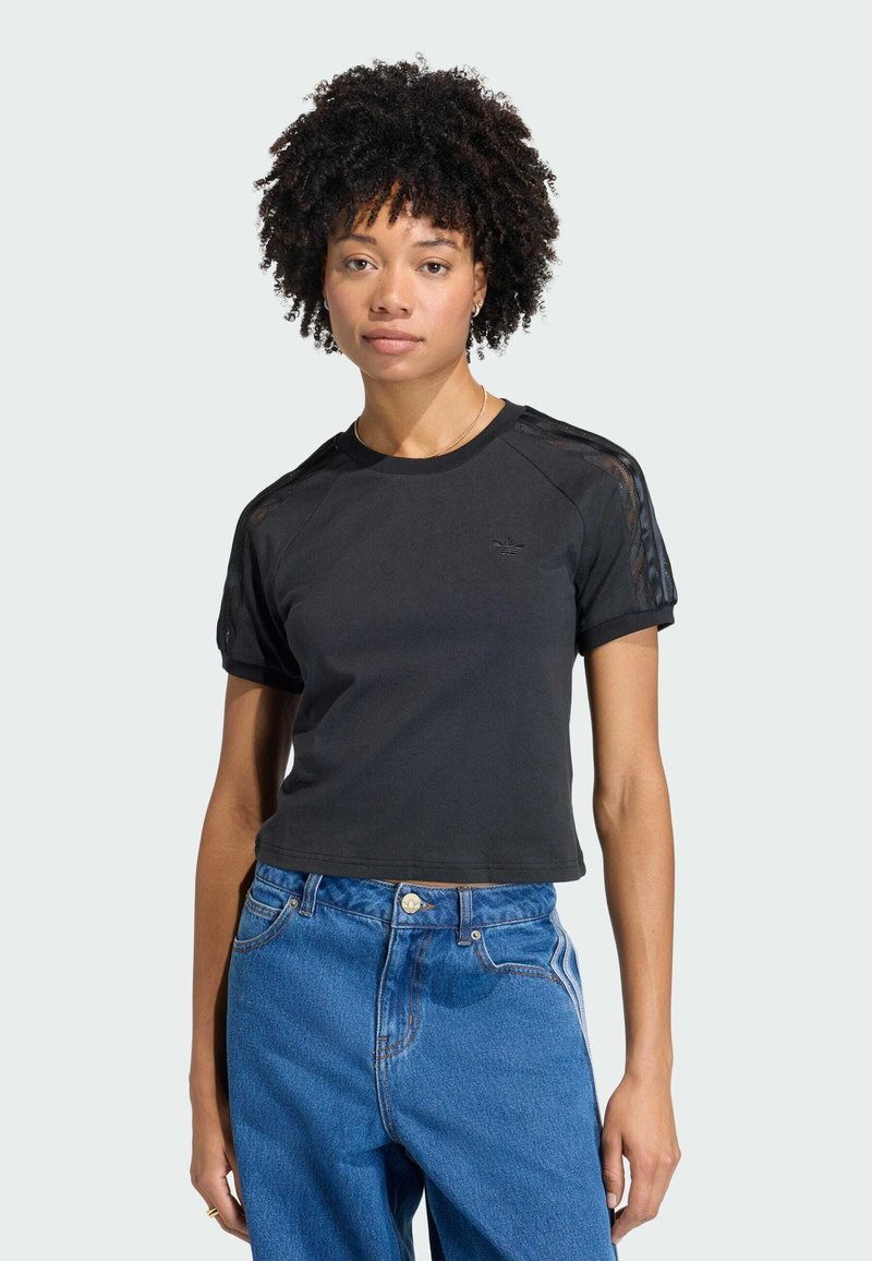 T-shirt court noir à manches courtes, avec des accents en maille sur les épaules et un petit logo. Associé à un jean bleu taille haute.