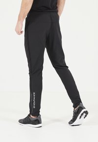 Svarta träningstights med slim fit, med en vit "ENDURANCE" logotyp, sidostråk och elastisk midja, tillsammans med svarta sneakers.