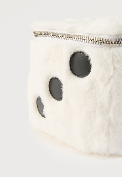 Κοντινό πλάνο σε λευκό, αφράτο ύφασμα θήκης με ασημένιο φερμουάρ και τρεις μαύρες δερμάτινες κυκλικές επιθέματα στο πλάι.