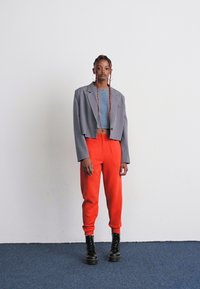 Grijze cropped blazer over een blauwe crop top, gecombineerd met felrode joggerbroek en zwarte chunky platformlaarzen. Effen kleuren, minimalistisch design.