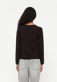 Suéter de manga longa castanho-escuro com decote redondo e mangas raglan, feito de um material de malha suave; combinado com jeans cinza-claro.