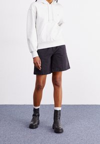 Šedá mikina s kapucí a přední kapsou, doplněná černými džínovými kraťasy. Černé kotníkové boty s texturovanou podrážkou a bílými lemy.