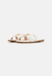 Vita platta sandaler gjorda av konstläder, med två breda remmar och en dekorativ spänne i guldton. Slät yta med en brun sula.