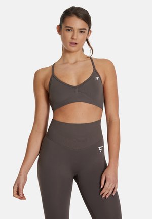 Donkerbruine sport-bh met dunne bandjes, een uitgesneden ontwerp en subtiele logo-detail; gecombineerd met hoge taille leggings in dezelfde kleur.