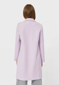 Ljuslila lång kappa i texturerat material, med rak silhuett, slagkrage och minimala sömnadsdetaljer bak.