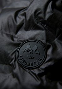 Svart, texturerad tyg med ett runt gummimärke präglat med flaggor och texten "LINDBERGH 1927" på en skrynklig yta.