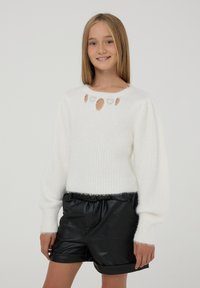 Biały sweter dziany z okrągłym dekoltem i wyciętymi sercami. Połączony z czarnymi szortami z eco-skóry i ściągaczami.