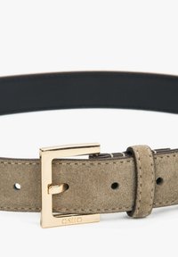 Suède riem in lichtbruin met een gladde textuur, voorzien van een gouden metalen gesp en stiksels. Verstelbaar met meerdere gaten.