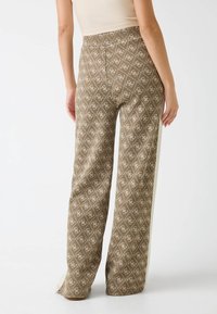 Brązowe szerokie spodnie w wzory z motywem diamentów i białymi akcentami; wykonane z teksturowanej tkaniny z detalami po bokach.
