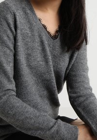 Szary wełniany sweter z dekoltem V i ozdobnymi czarnymi koronkami przy kołnierzu. Długie rękawy i teksturowany materiał.