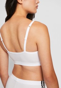Bralette branco em algodão com alças ajustáveis e um design simples. O tecido é suave e elástico, apresentando um nas costas sem costuras e hardware mínimo.