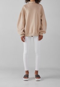 Beige oversize sweatshirt med långa ärmar och hög hals; kombinerad med vita tajta byxor och gråa platåskor. Slät textur överallt.