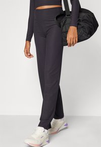 Sorte ribbede leggings med høj talje, parret med en sort taske. Sneakers er hvide med lilla accenter og teksturerede detaljer.
