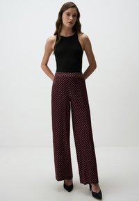 Zwarte geribbelde tanktop gecombineerd met wijde broek met een rood en marineblauw geometrisch patroon, een gladde textuur en een aansluitende tailleband.