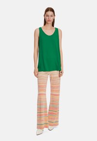 Green sleeveless top paired with patterned, flared pants featuring pink, yellow, blue, and white zigzag designs. Smooth fabric texture.