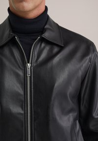 Chaqueta de piel negra con un diseño elegante, que cuenta con cierre de cremallera y cuello de punta. Textura suave y acabado mate.
