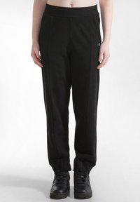 Schwarze Sporthosen aus weichem Stoff, mit einem breiten elastischen Bund, zwei Seitennähten und einem kleinen Logo auf der linken Seite.