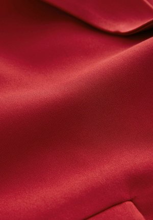 Sarkans audums ar gludu tekstūru, kas demostrē vieglu spīdumu. Virsma ir smalki audumā, izceļot smalkus rakstus un strukturētu izskatu.