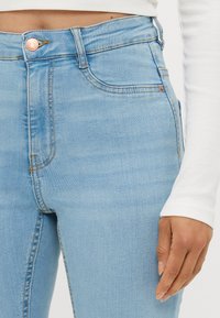 Lyseblå denimjeans har høy midje, subtile slitasjer, kobberknappdetaljer og standard fem-lommers design.