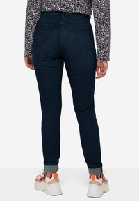 Jeans ajustados de color azul oscuro con cinco bolsillos, detalles de costura sutiles y dobladillos enrollados, combinados con zapatillas blancas con acentos naranjas.