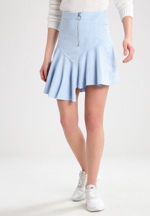 Gonna azzurro chiaro a campana realizzata in materiale morbido simile alla pelle scamosciata, con zip frontale e cuciture angolate, abbinata a sneakers bianche da ginnastica.