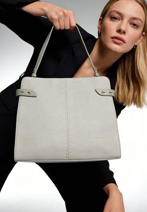 Blonde Frau in Schwarz hält eine große hellgraue Lederhandtasche mit obenliegenden Griffen und kleinem goldenen Logo vorne.