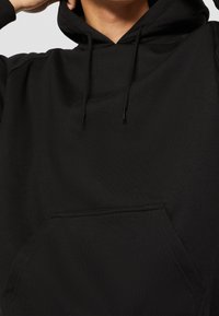 Černá mikina s kapucí vyrobená z měkké bavlny, s přední kapsou, stahovací kapucí a hladkým povrchem. Minimalistický design bez vzorů.