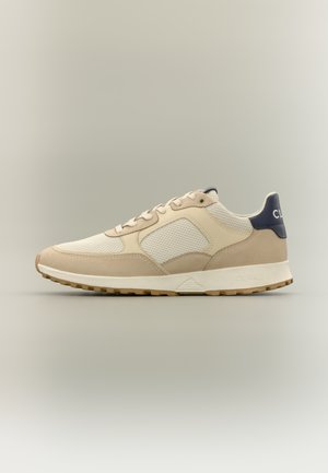 Beige og cremefarvet lavtop-sneaker med mesh- og ruskindspaneler, beige snørebånd, hvid sål og navy hælflap med mærkedetalje.