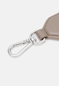 Jasno taupe skórzany brelok z metalowymi srebrnymi elementami, wyposażony w sprężynowy zatrzask i gładką teksturę, z precyzyjnym przeszyciem.