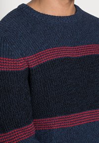 Maglione blu navy lavorato a maglia con una finitura testurizzata, con strisce rosse orizzontali sul petto e sulle spalle, design con collo rotondo.