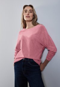 Maglione a maniche lunghe rosa chiaro con una vestibilità comoda, texture morbida e scollatura ampia, abbinato a jeans blu scuro.