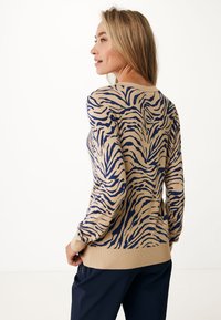 Beige tröja med marinblå tigerstrecksmönster, ribbade muddara och nederkant, rund halsringning, mjuk textur, figurnära silhuett, bakvy.