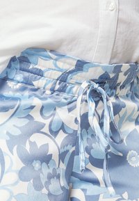 Calças com padrão floral em tons de azul e branco, com uma cintura elástica e cordão para ajuste. Textura suave.