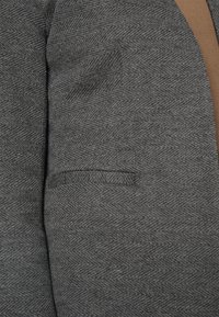 Grijs vissengraatblazerstof met een subtiele textuur. Beschikt over een slanke notch-lapel en een zijzak met paspel.