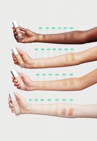 Fyra armar håller foundationflaskor som visar olika nyanser från mörk till ljus. Varje nyans är märkt med nummer ovanför prov på huden.