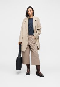 Beige coat, navy top, and tan cropped pants. Brown leather boots and black tote bag complete the look with minimalist design and relaxed fit.