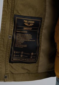 Étiquette de la veste PME Legend Cargoyet indiquant le mélange de tissus, les caractéristiques comme les poignets réglables, la doublure en coton respirante et la finition durable effet pierre lavée.