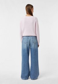 Jasnoróżowy sweter dzianinowy z długim rękawem zestawiony z luźnymi, wyblakłymi niebieskimi dżinsami typu wide-leg z dwoma tylnymi kieszeniami.