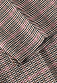 Tkanina s tkaným vzorem houndstooth v hnědé, černé a bílé barvě s růžovými akcenty; texturovaný povrch, viditelné skládací části.