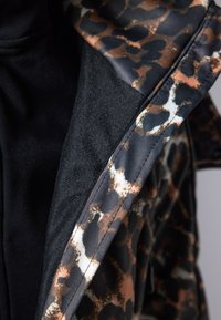 Innside av jakken med svart og brunt leopardmønster, med et mykt svart tekstil og detaljerte sømmer langs kantene.
