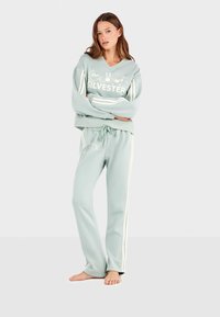 Mintgroen lounge-outfit bestaande uit een V-hals sweatshirt met de print "SILVESTER" en bijpassende broek met zijstrepen en een rozenontwerp.