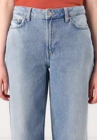 Jean taille haute bleu clair en denim, avec une coupe droite, cinq poches et des détails légèrement décolorés sur le tissu.