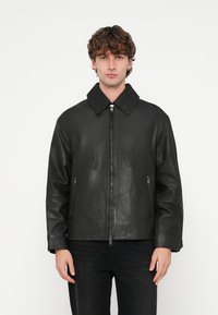 Veste en cuir noir avec un large col, une fermeture éclair frontale et deux poches zippées. Le design présente une texture lisse et une coupe décontractée.
