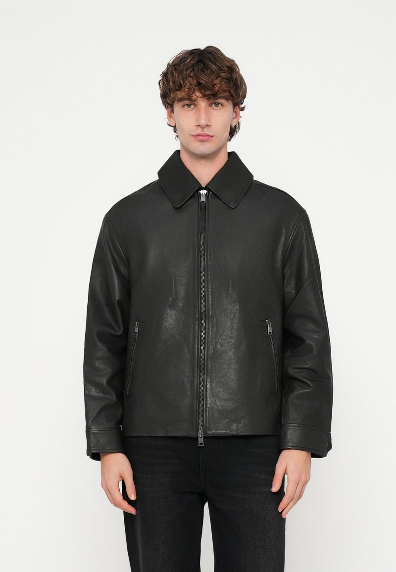 Veste en cuir noir avec un large col, une fermeture éclair frontale et deux poches zippées. Le design présente une texture lisse et une coupe décontractée.