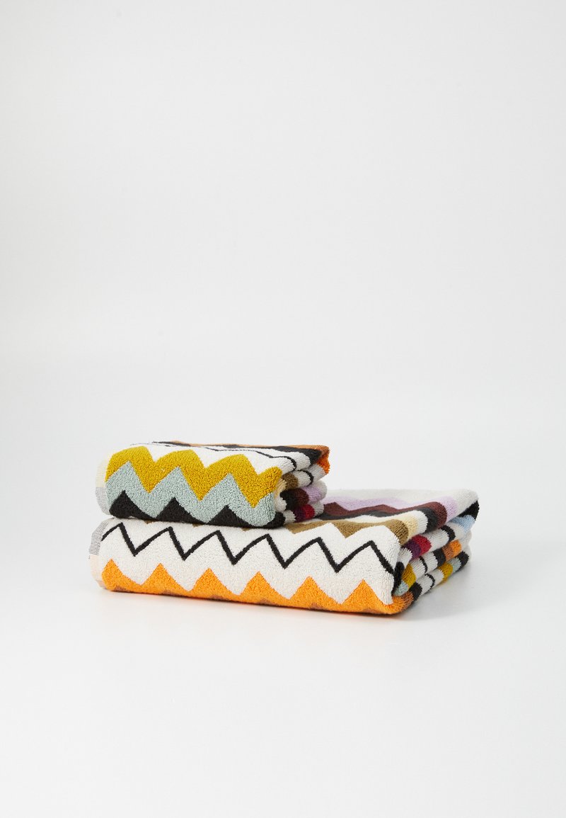Dve zložene brisače z zigzag vzorcem v rumeni, oranžni, črni in pastelnih barvah. Teksturna bombažna tkanina, pravokotna oblika.