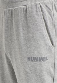 Grå joggebukser lavet af blødt stof, med sidelommer og ribbet talje. "HUMMEL" logoet trykt i mørkegrå på låret.
